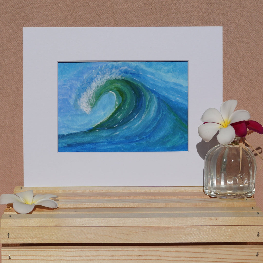 A square art print depicting a blue and green ocean wave, styled on a light wood crate with white flowers against a draped beige fabric backdrop.