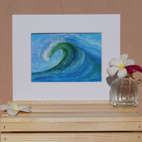 A square art print depicting a blue and green ocean wave, styled on a light wood crate with white flowers against a draped beige fabric backdrop.